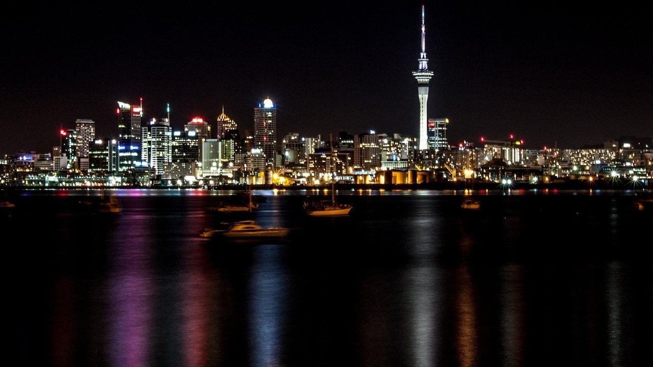 Auckland city skyline and the Sky Tower lit up at night, reflected in the harbour